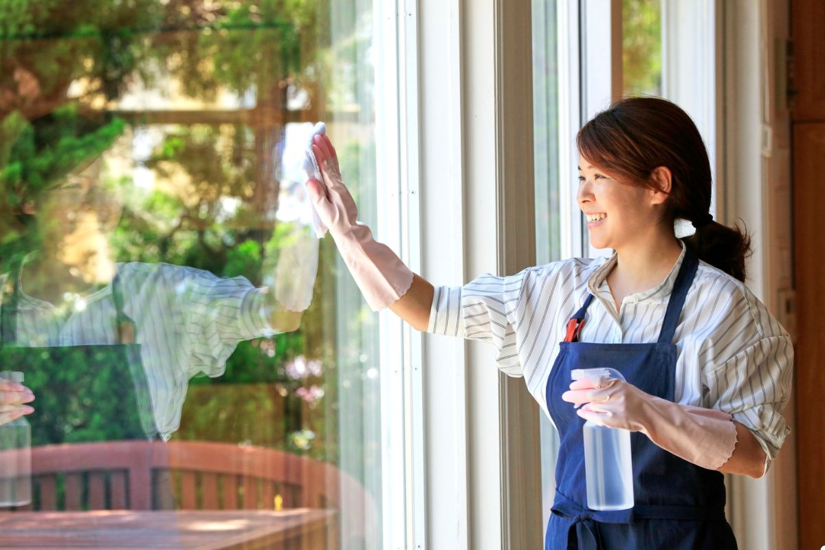 A woman in an apron diligently cleans a window, showcasing her commitment to maintaining a tidy home environment.
