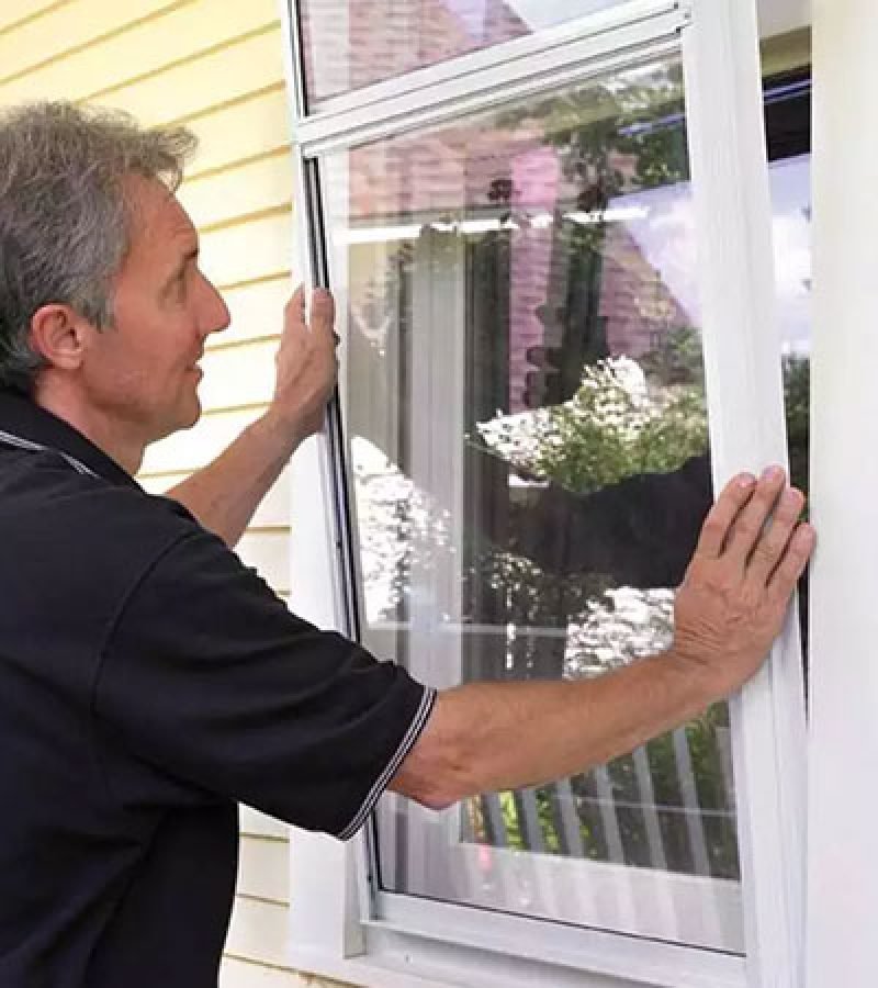 A man is preparing to install a screen by opening a window for the Storm Window Cleaning Service.